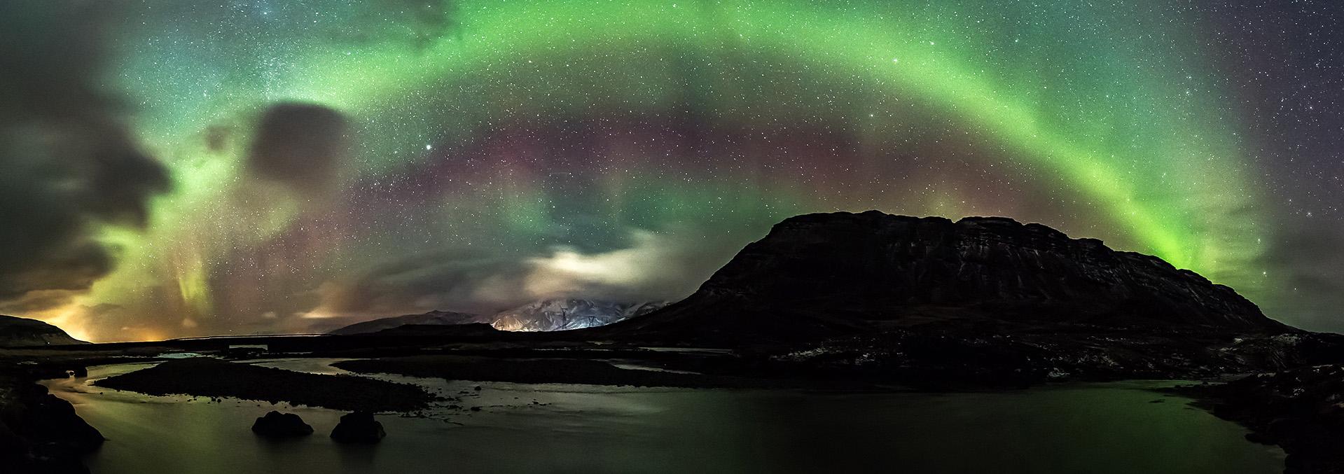 Rocky landscape at night with green and purple aurora lights glowing in the dark sky