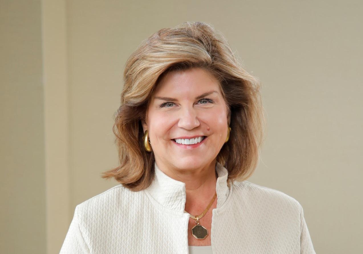 Women with shoulder length hair and a cream suit jacket smiles