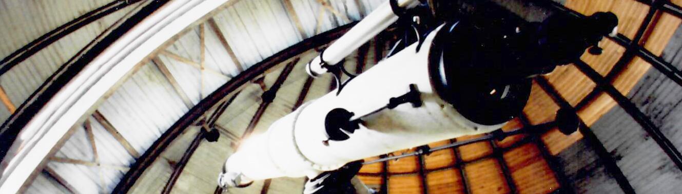 White telescope points up at closed, wooden observatory dome that is not the best shape with section unpainted and peeling in areas.