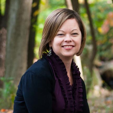 Woman with short brown hair in black shrug with purple shirt smiles