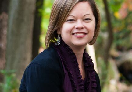 Woman with short brown hair in black shrug with purple shirt smiles