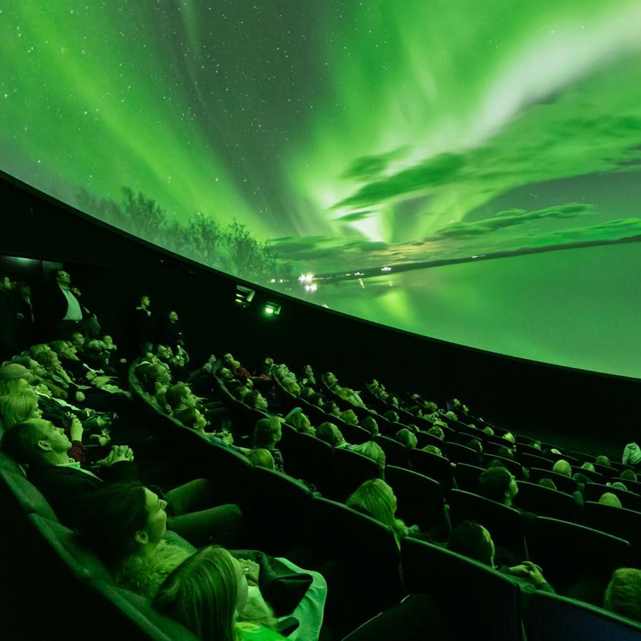 Audience looks up at domed shaped image depicting bright green lights in the sky over a snowy landscape