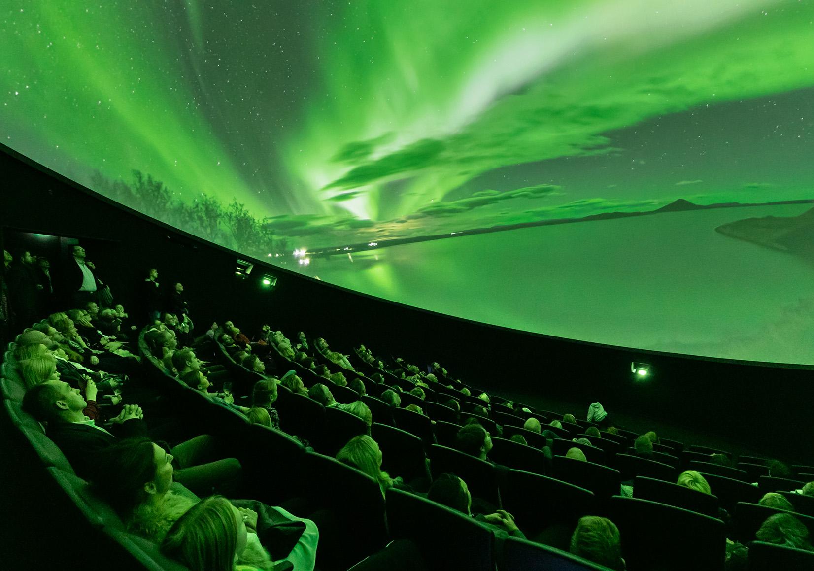 Audience looks up at domed shaped image depicting bright green lights in the sky over a snowy landscape
