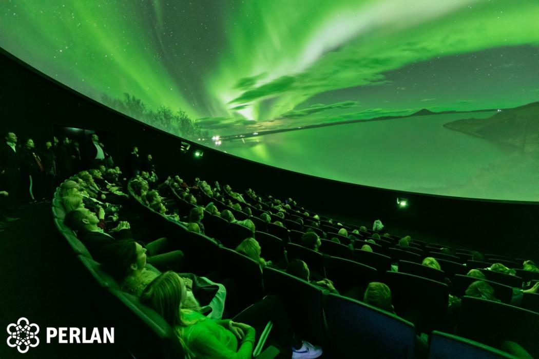 Audience looks up at domed shaped image depicting bright green lights in the sky over a snowy landscape