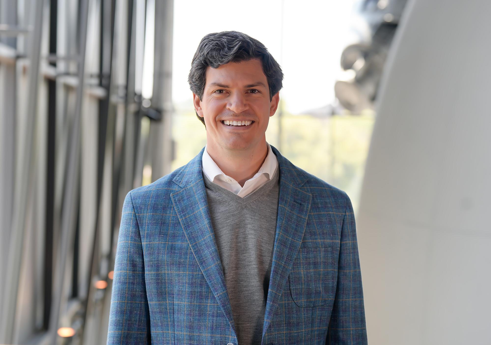 Man in light blue plaid jacket with gray shirt smiles