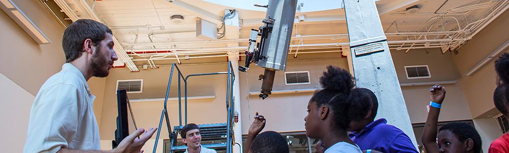 Museum observatory educators speak to a group of students with the observatory telescope in the background