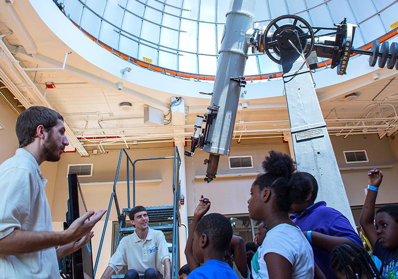 Museum observatory educators speak to a group of students with the observatory telescope in the background