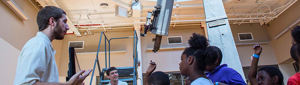 Museum observatory educators speak to a group of students with the observatory telescope in the background