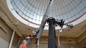 Individual standing on a ladder looking through the Alvan Clark telescope