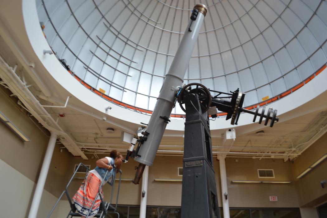 Individual standing on a ladder looking through the Alvan Clark telescope