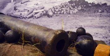 Large antique cannon on exhibition with photo backdrop of a destroyed Main St. in Columbia, SC c. 1865