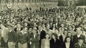 Large group gathered outside with side of textile mill building to the left with decorative patriotic banners on the windows