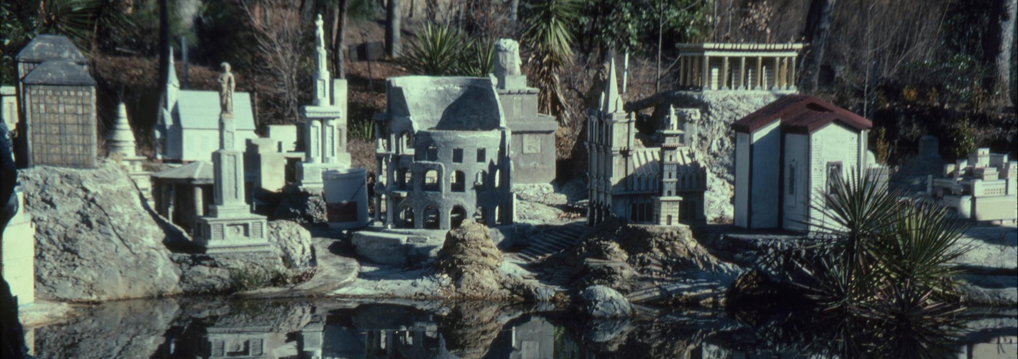 Collection of large building replicas of classical architecture made in concrete set up outdoors with a small pond in the foreground