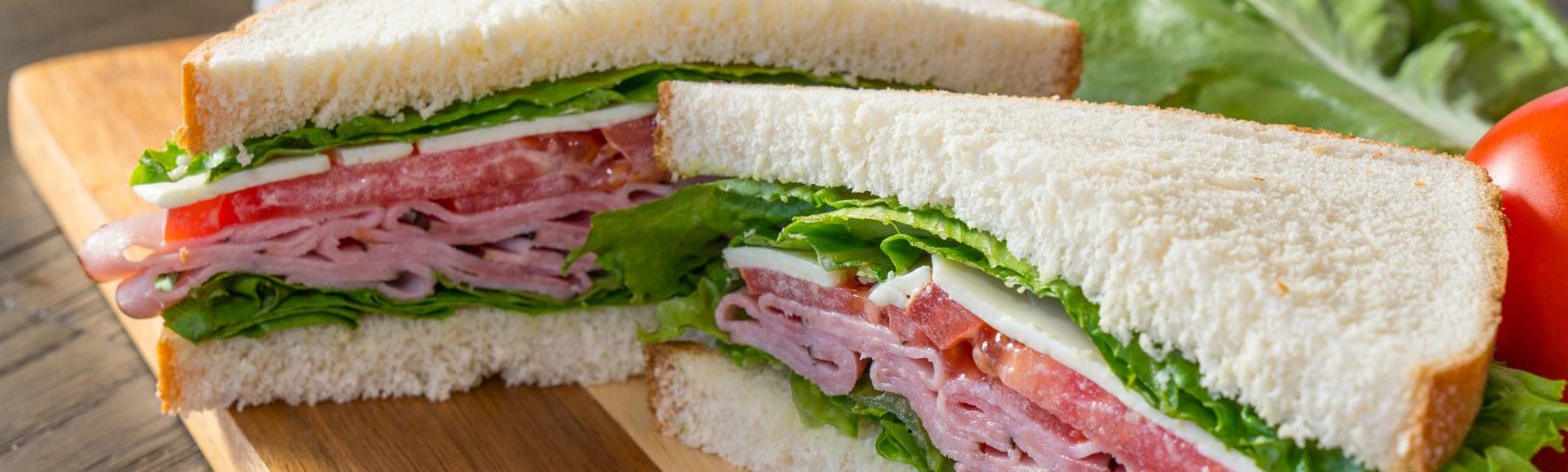 White bread sandwich cut into triangles with ham, tomato, cheese lettuce