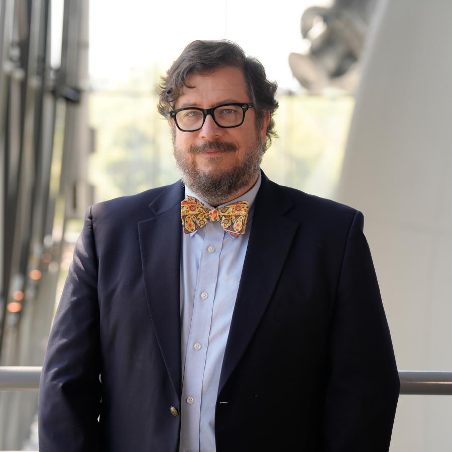 Man with beard in navy jacket and yellow bow tie smiles at camera