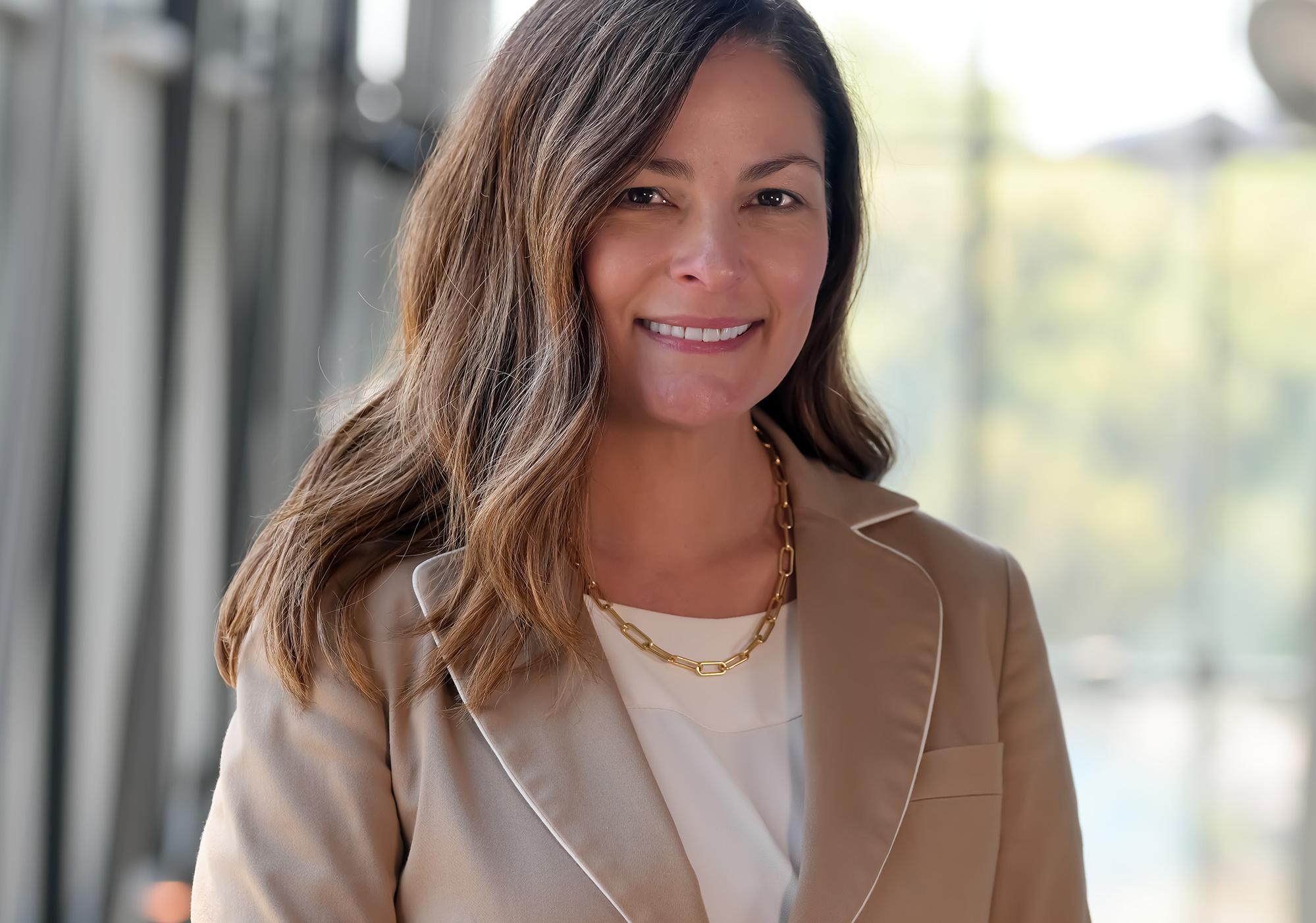 Woman with long brown hair in tan blazer smiles