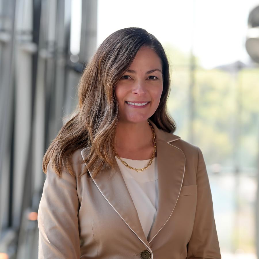 Woman with long brown hair in tan blazer smiles