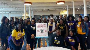 Large group of young people wearing yellow and purple accented clothing stand around a sign that reads: Douglass Day.