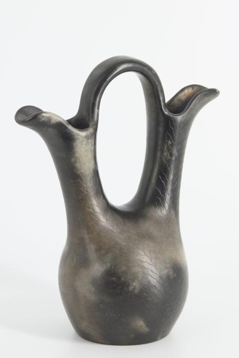Horse pot created by applying a horse head and neck to one side of a four footed pot and a tail-like handle on the opposite side. The pot is predominantly dark with orange accents around the edge of the opening and the tail. The horse's head and mane have incised detailing, as well as an incised blanket on either side of the opening. There is a smaller blanket incised around the handle.
