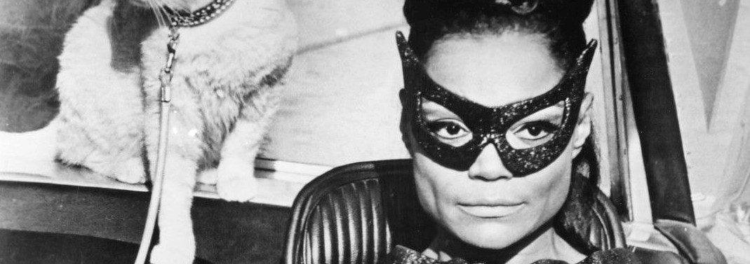 Eartha Kitt in Catwomen costume driving a car with a white cat behind her