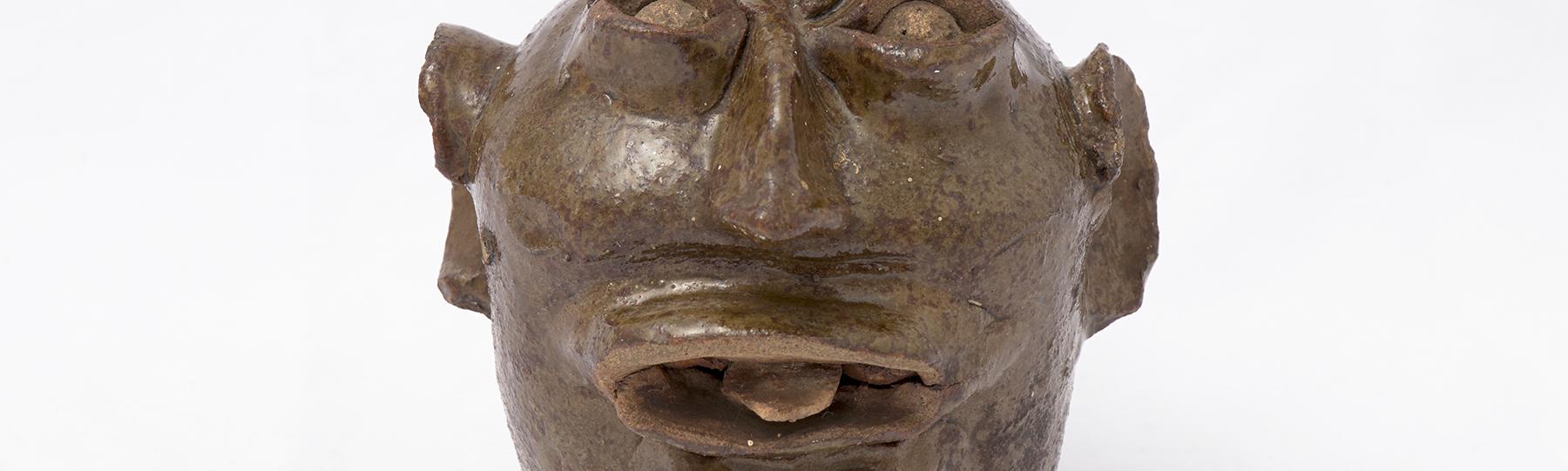 Ceramic vessel in the shape of a face with large ear and a protruding tongue
