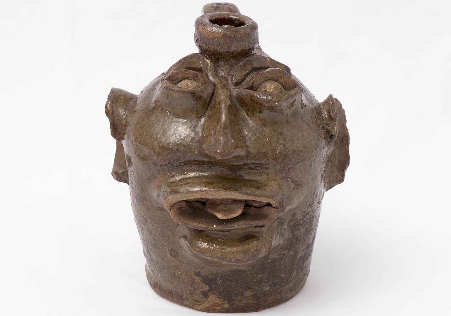 Ceramic vessel in the shape of a face with large ear and a protruding tongue