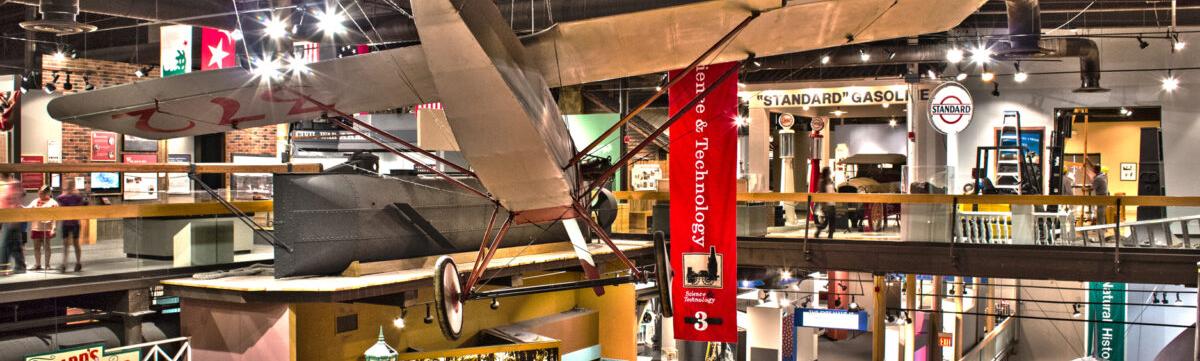 View of third and four floor exhibition galleries with biplane hanging from ceiling in the foreground