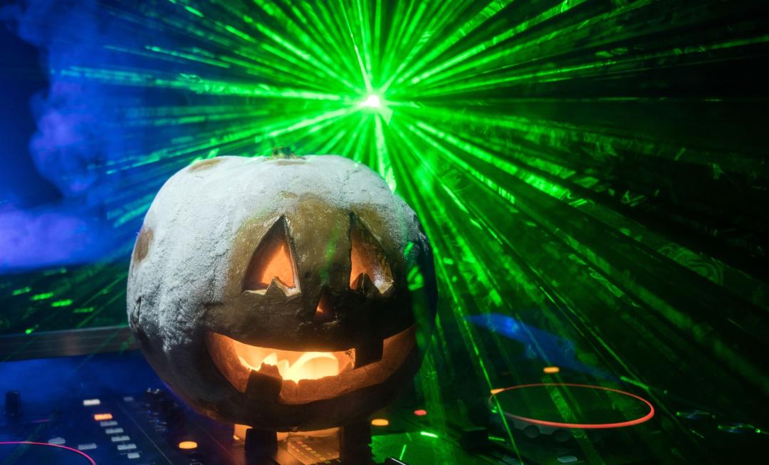 Jack O lantern sitting on DJ turntables with green lasers behind it