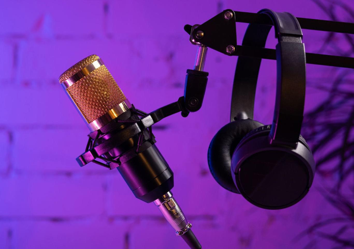 Headphones hang on a microphone stand with a purple and blue wall in the background