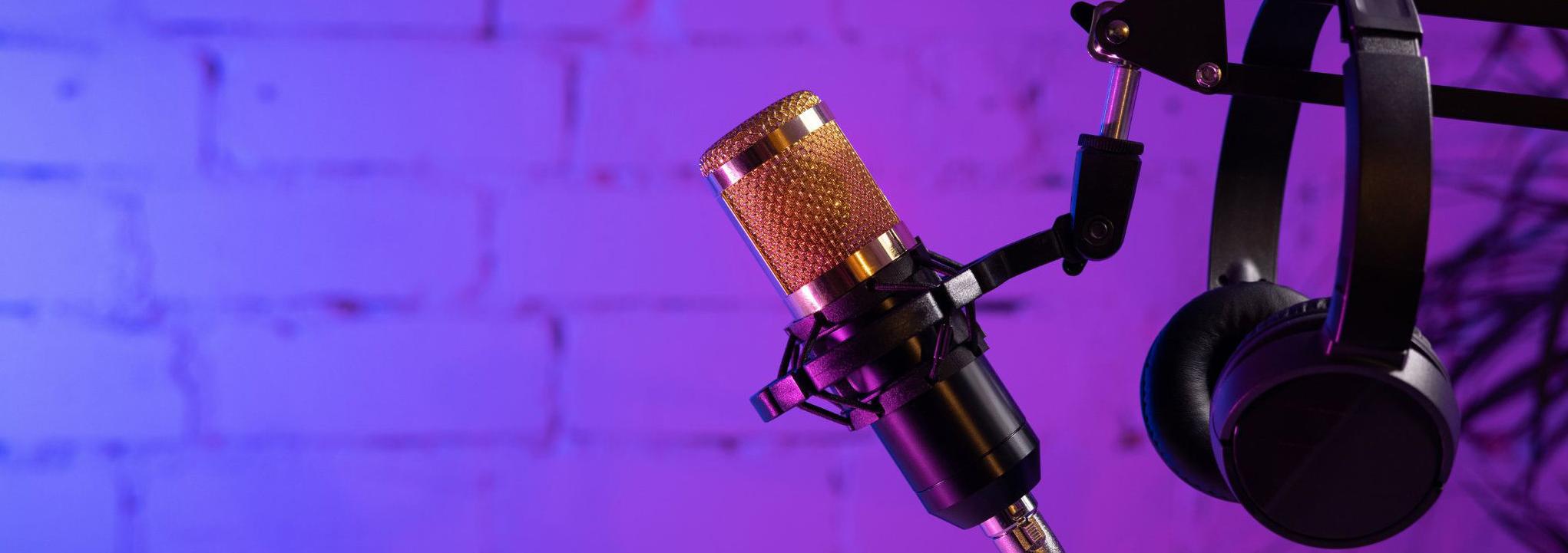 Headphones hang on a microphone stand with a purple and blue wall in the background