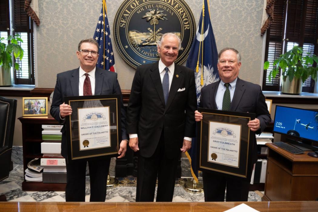 Three men standing, two holding awards
