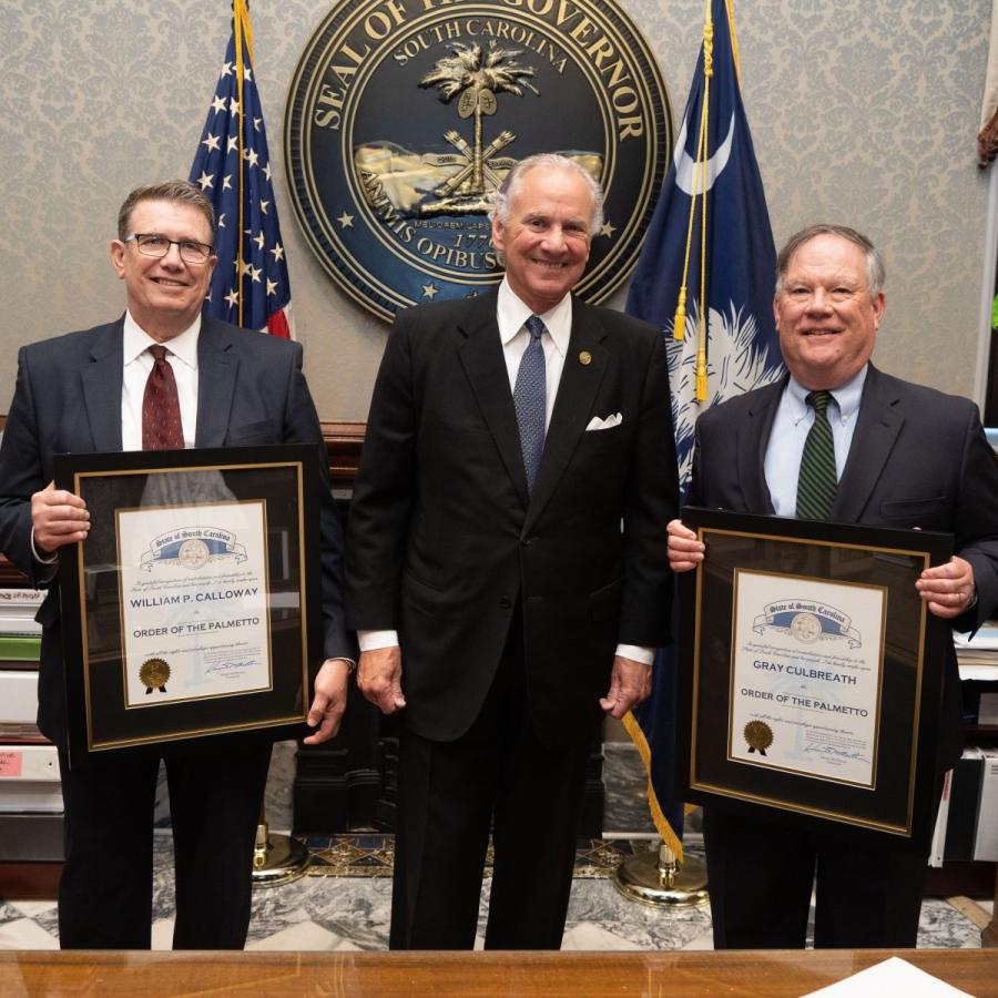 Three men standing, two holding awards