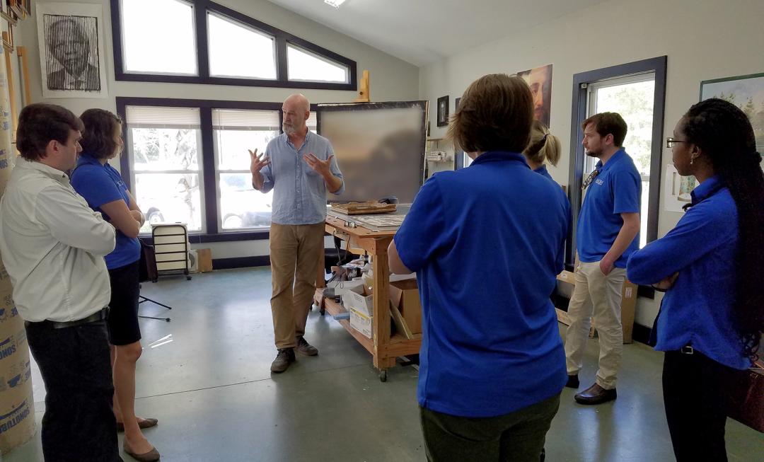 Individuals stand around a studio to see the action of action of restoring a newly acquired piece art 