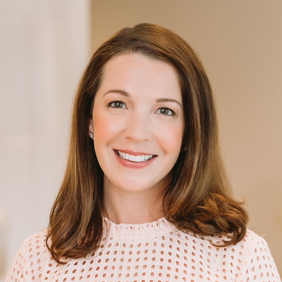 Woman with medium length brown hair wearing a white shirt smiles