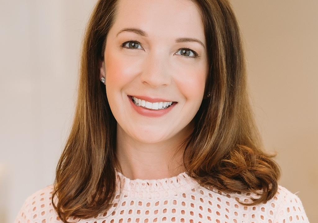 Woman with medium length brown hair wearing a white shirt smiles