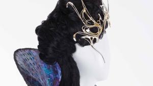 Mannequin in profile on white background with dark wig wearing Twisty and spiked metal crown and a purple and gold dress