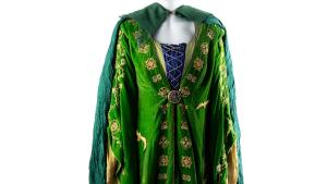 Mannequin on a white background wearing a loose and flowy green velvet dress with gold embroidered detailing and a green cape.
