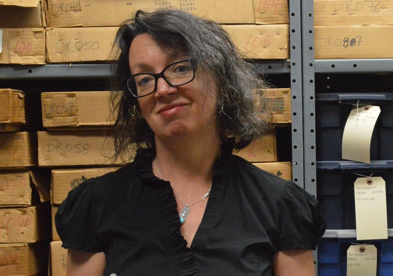 Woman in glasses with short gray and brown hair in a Black shirt holds a pottery sherd