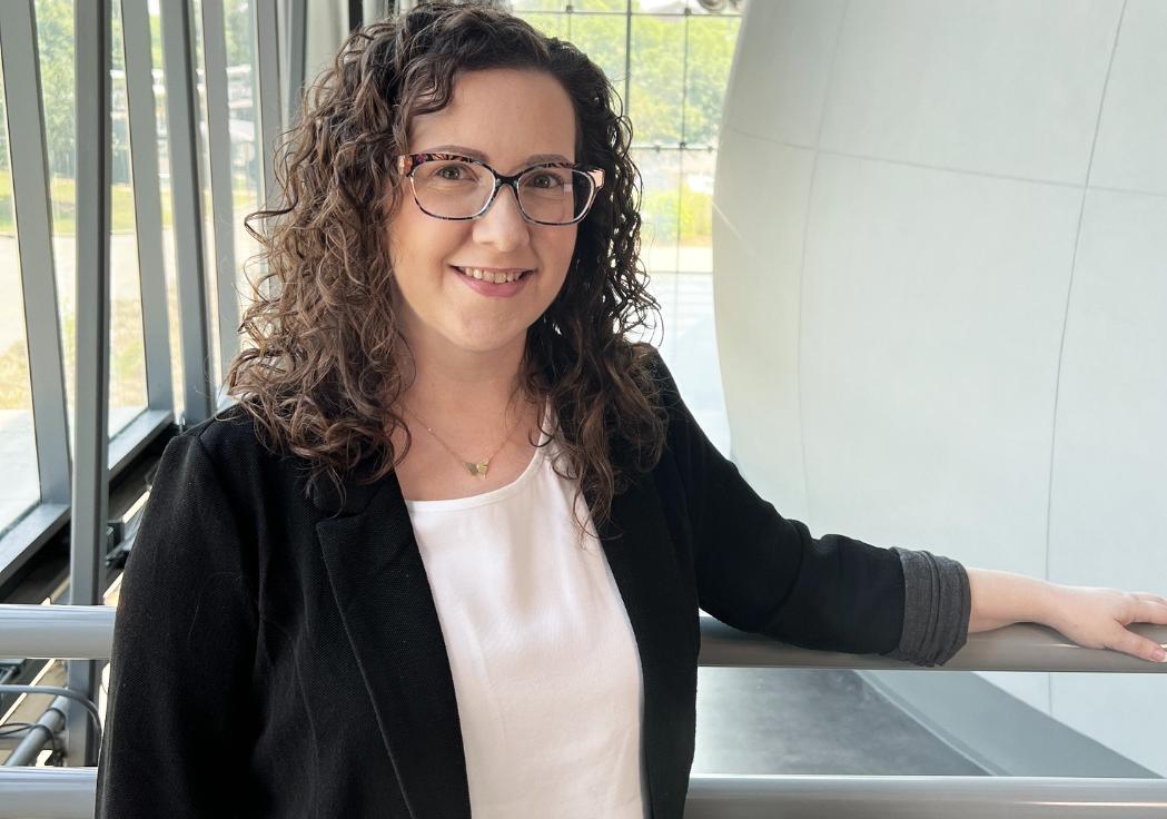 Woman with curly brown hair and a black suit jacket smiles