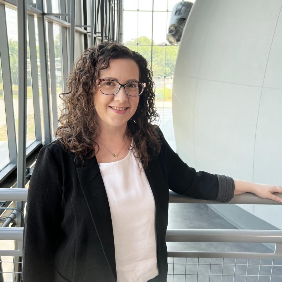 Woman with curly brown hair and a black suit jacket smiles
