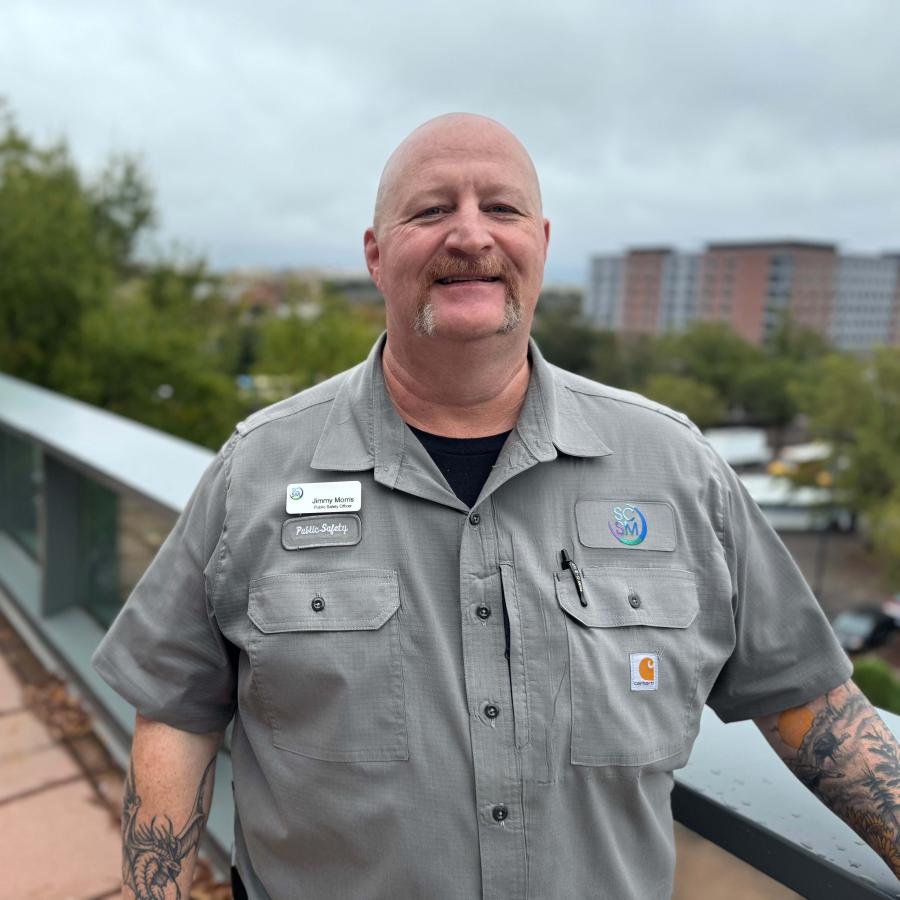 Man stands on balcony wearing a taupe shirt and nametag