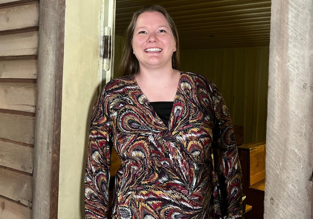 Woman with light brown hair and patterned brown dress smiles at camera