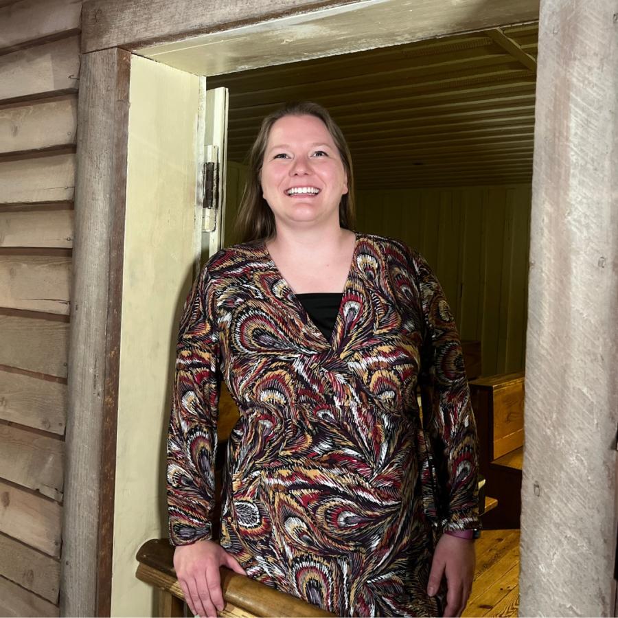 Woman with light brown hair and patterned brown dress smiles at camera