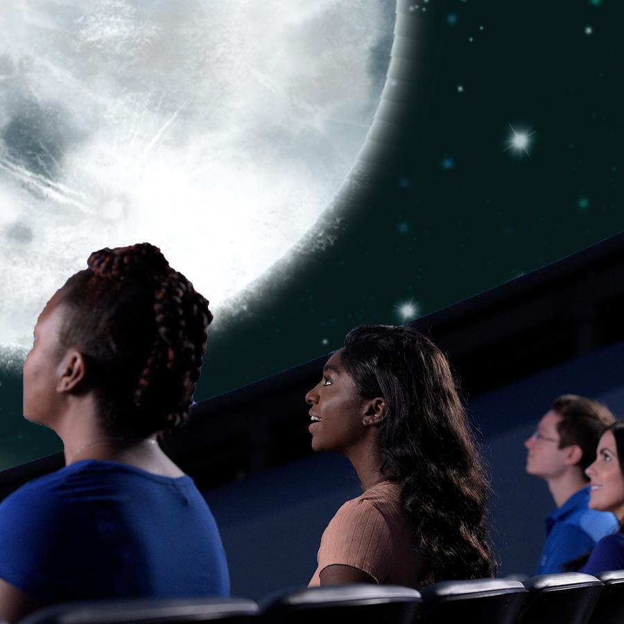 Individuals seated in theater looking up at an image of the moon
