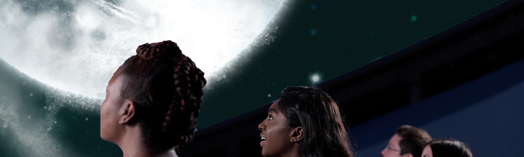 Individuals seated in theater looking up at an image of the moon