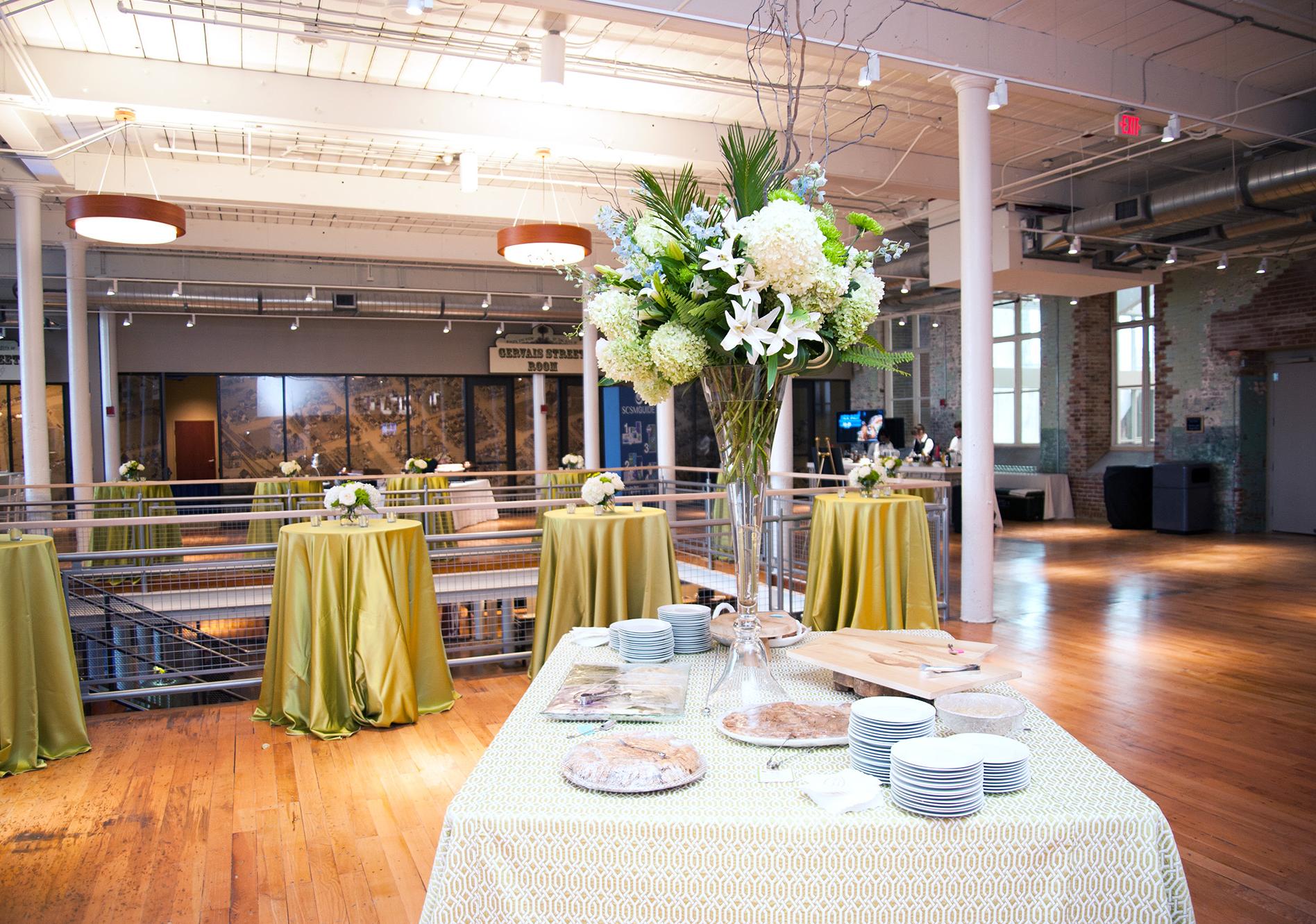 Table with white tablecloth and white dishes with Large white floral arrangement set up in an open space with wood flooring