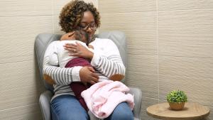Mother sits in chair with baby cradled against her chest