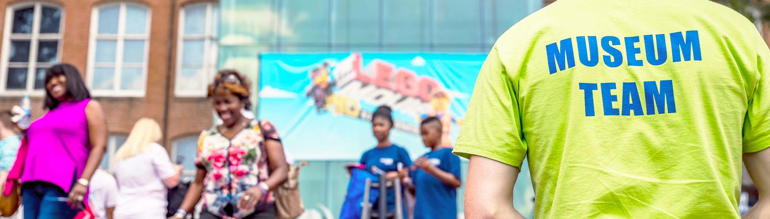 Man faces away from camera in neon yellow shirt with "Museum Team" written across the back in blue letters
