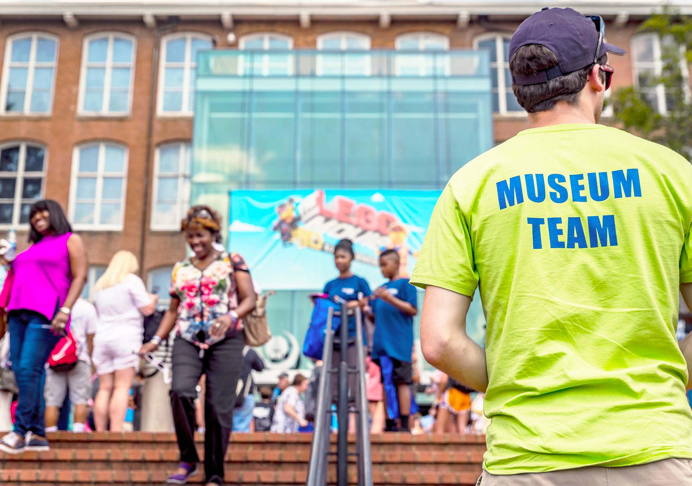 Man faces away from camera in neon yellow shirt with "Museum Team" written across the back in blue letters