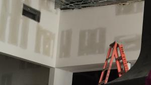 Two museum staff members, a man and a woman, in hard hats stand with back to camera facing a large black metal base being lowered down onto a concrete pier.